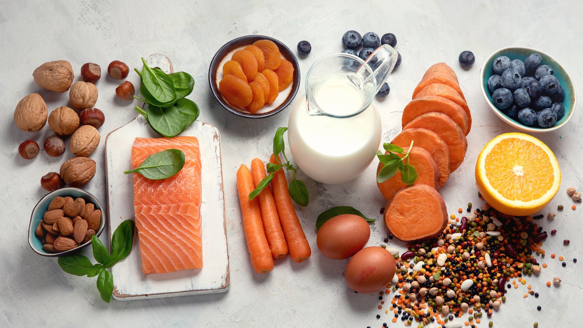 A well-lit, high-resolution close-up photograph of a variety of fresh, vibrant fruits and vegetables arranged in a visually appealing still life composition. The produce items should include a selection of eye-healthy foods such as carrots, leafy greens, citrus fruits, bell peppers, and blueberries. The arrangement should be placed on a neutral, slightly reflective surface, with soft, natural lighting falling upon the scene from the side, creating subtle shadows and highlights that enhance the texture and colors of the healthy ingredients. The overall mood should convey a sense of nourishment, vitality, and the importance of a balanced, eye-supportive diet. Foods That Boost Eye Health 03